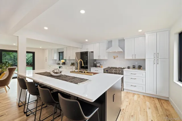 a kitchen with stainless steel appliances kitchen island granite countertop a stove a sink a refrigerator and white cabinets with wooden floor