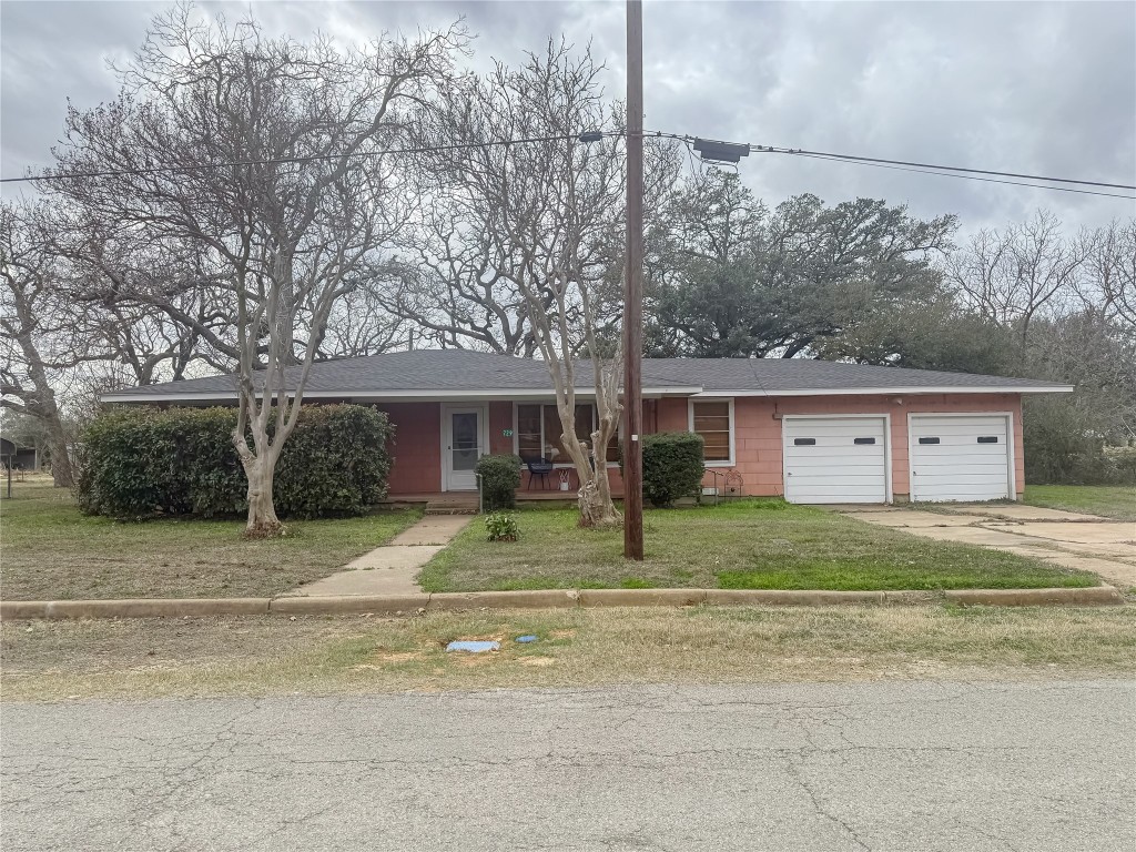 729 Main Street Lexington, TX 78947 - Photo 15 of 15 Single story home featuring concrete driveway, covered porch, a front lawn, an attached 2 car garage, and a shingled roof