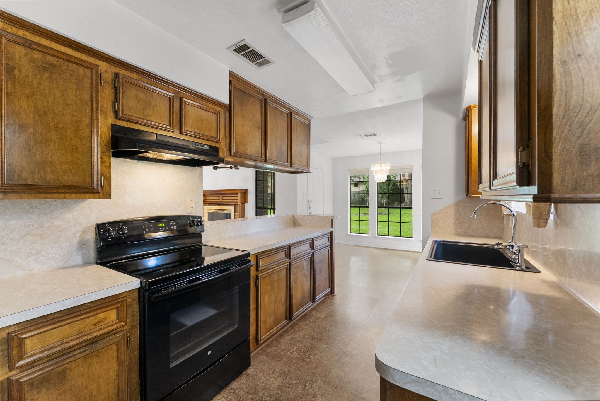 202 Sunset Boulevard Conroe, TX 77303 - Photo 18 of 50 This inviting kitchen features warm wooden cabinetry, sleek countertops, and a modern black stove, all beautifully illuminated by natural light streaming through large windows, creating a cozy yet functional space perfect for culinary creativity.