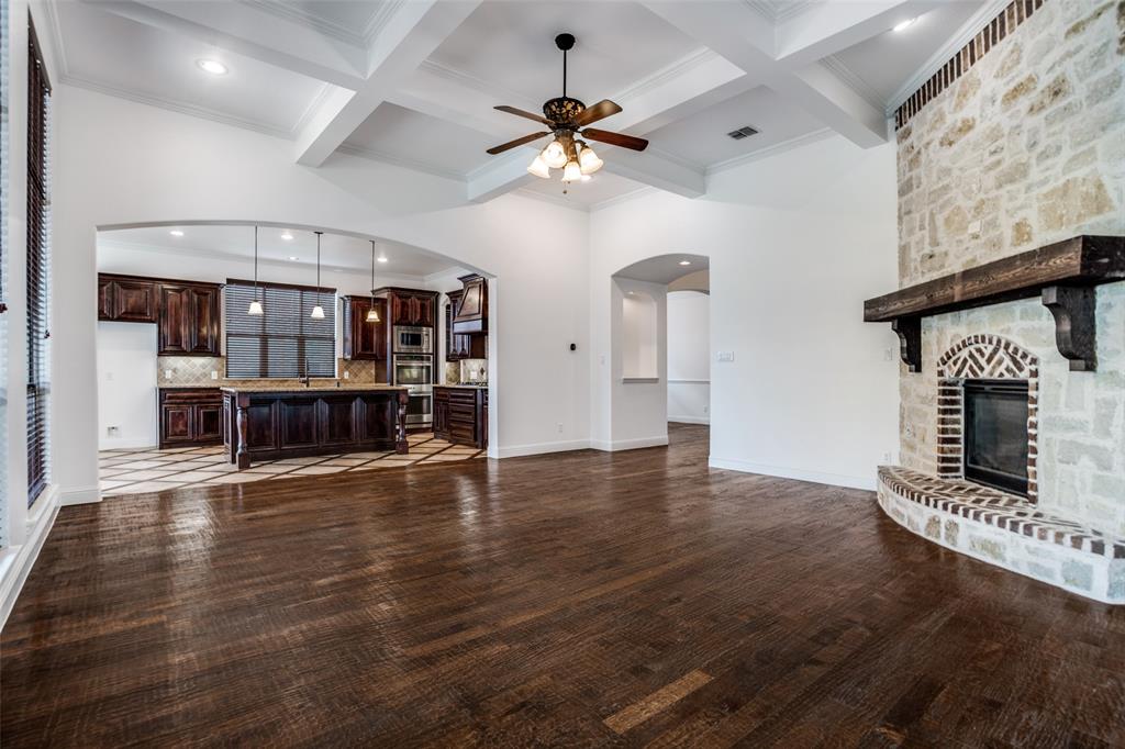 900 Jessica Lane Prosper, TX 75078 - Photo 15 of 40 an empty room with wooden floor a ceiling fan a kitchen view and a fireplace