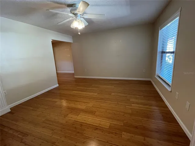 a view of an empty room with wooden floor and a chandelier fan