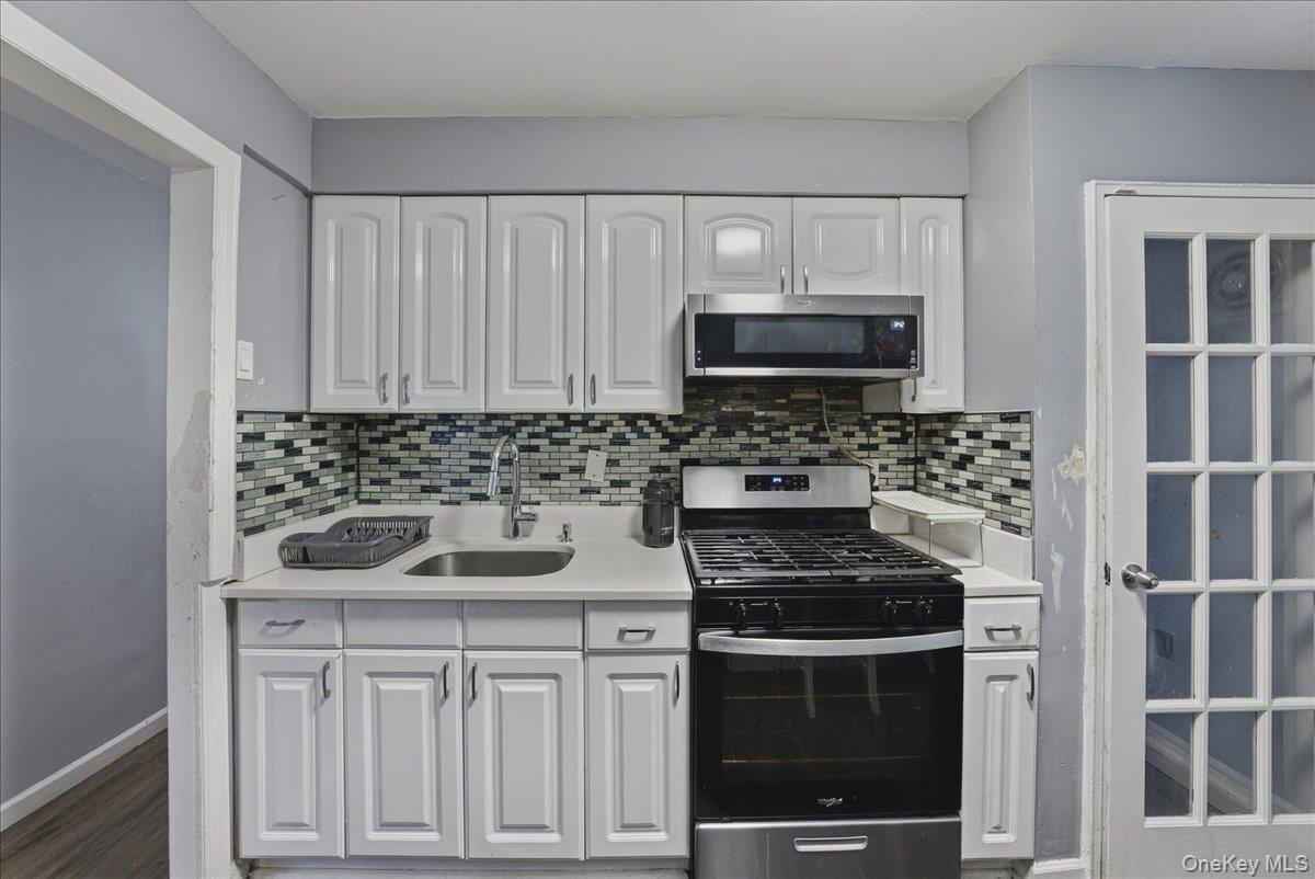 128-66 238th Street Queens, NY 11422 - Photo 9 of 25 a kitchen with white cabinets a stove and microwave