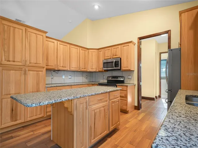 a kitchen with stainless steel appliances granite countertop a stove top oven a sink dishwasher and a refrigerator with wooden floor