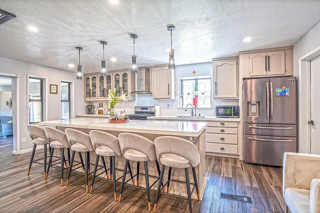 a kitchen with stainless steel appliances kitchen island granite countertop a refrigerator a stove and white cabinets with wooden floors