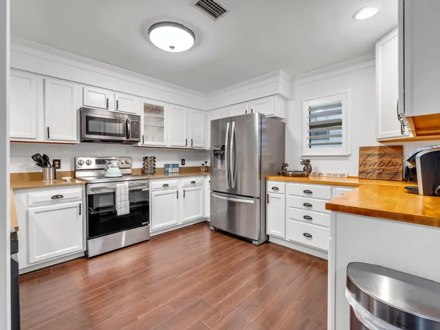 a kitchen with stainless steel appliances granite countertop a stove top oven a sink dishwasher and white cabinets with wooden floor