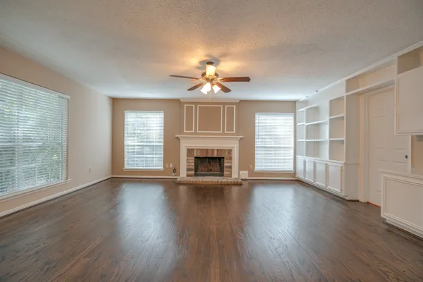 a view of an empty room with wooden floor and a kitchen
