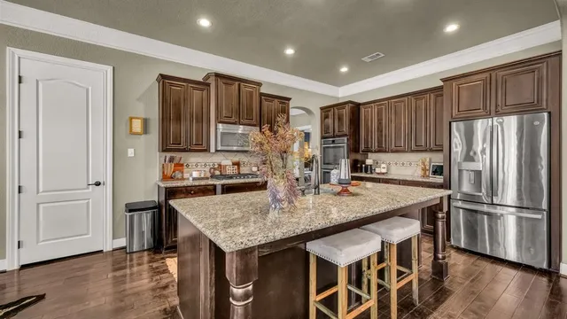 a kitchen with stainless steel appliances granite countertop a refrigerator a stove and a sink with wooden floor
