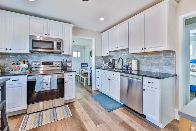 59 East 8680th Street South Sandy, UT 84070 - Photo 5 of 33 Kitchen featuring white cabinetry, dark countertops, wood-finish flooring, stainless steel appliances, and a subway tile backsplash