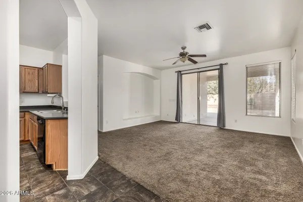 a view of an empty room with window and kitchen view