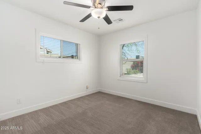 an empty room with chandelier fan and windows