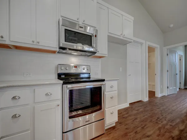 a kitchen with stainless steel appliances granite countertop a refrigerator a sink dishwasher a stove and white countertops with wooden floor