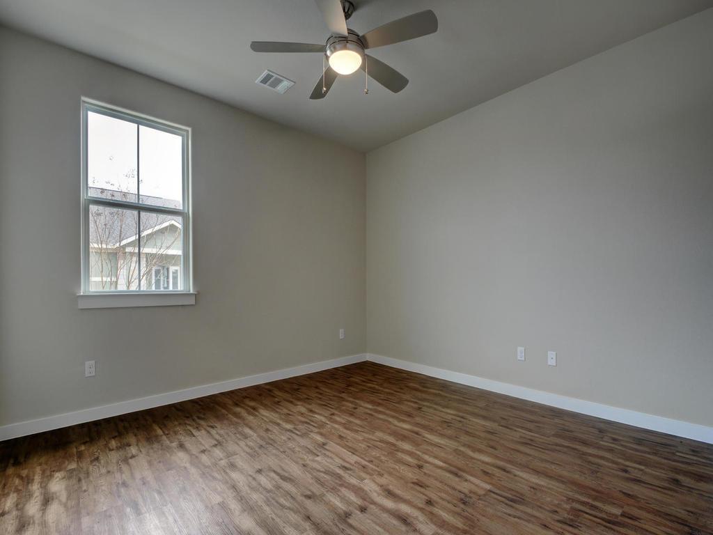 240 Rose Drive, Unit A Dripping Springs, TX 78620 - Photo 19 of 30 an empty room with wooden floor chandelier fan and windows