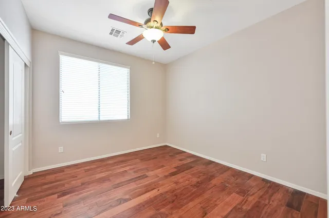 an empty room with wooden floor ceiling fan and windows