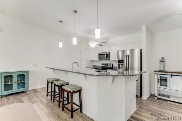 a kitchen with stainless steel appliances a microwave a stove a refrigerator a sink a dining table and chairs with wooden floor