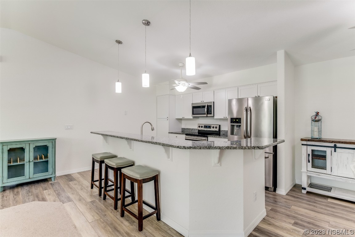 3129 Pine Tree Drive Edgewater, FL 32141 - Photo 7 of 34 a kitchen with stainless steel appliances a microwave a stove a refrigerator a sink a dining table and chairs with wooden floor
