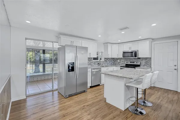 a kitchen with stainless steel appliances granite countertop a refrigerator a stove top oven and a sink with wooden floor