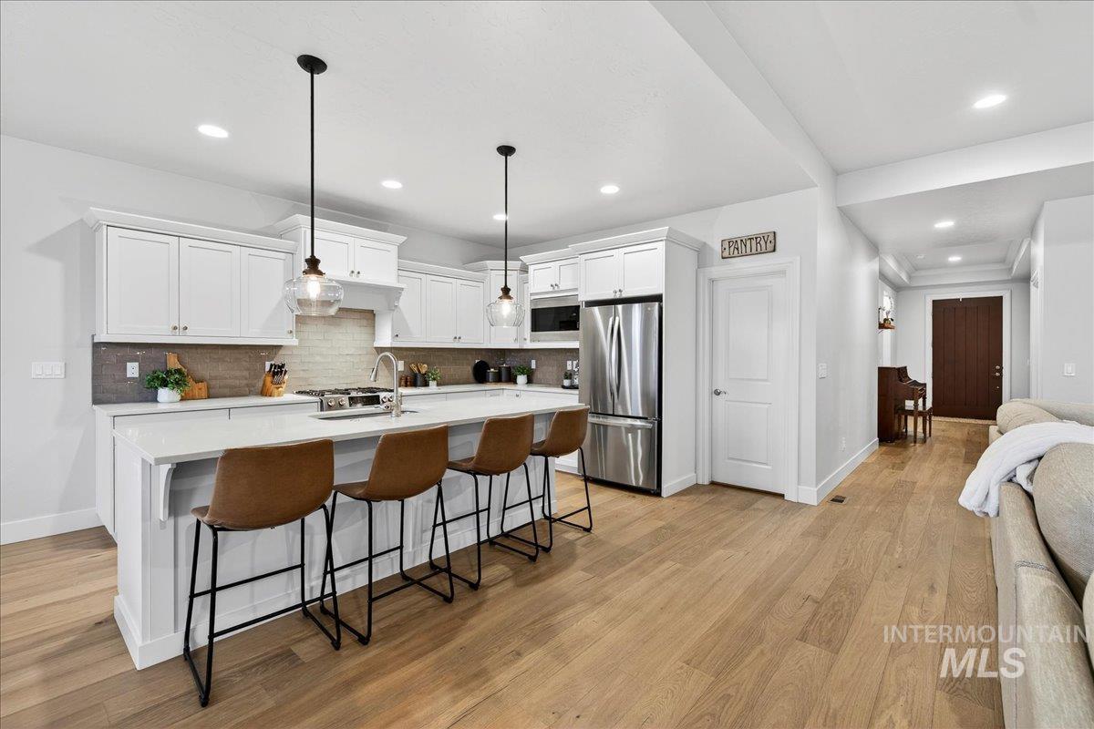24813 Valley Run Place Star, ID 83669 - Photo 11 of 50 Kitchen featuring a kitchen breakfast bar, white cabinetry, appliances with stainless steel finishes, a kitchen island with sink, and hanging light fixtures