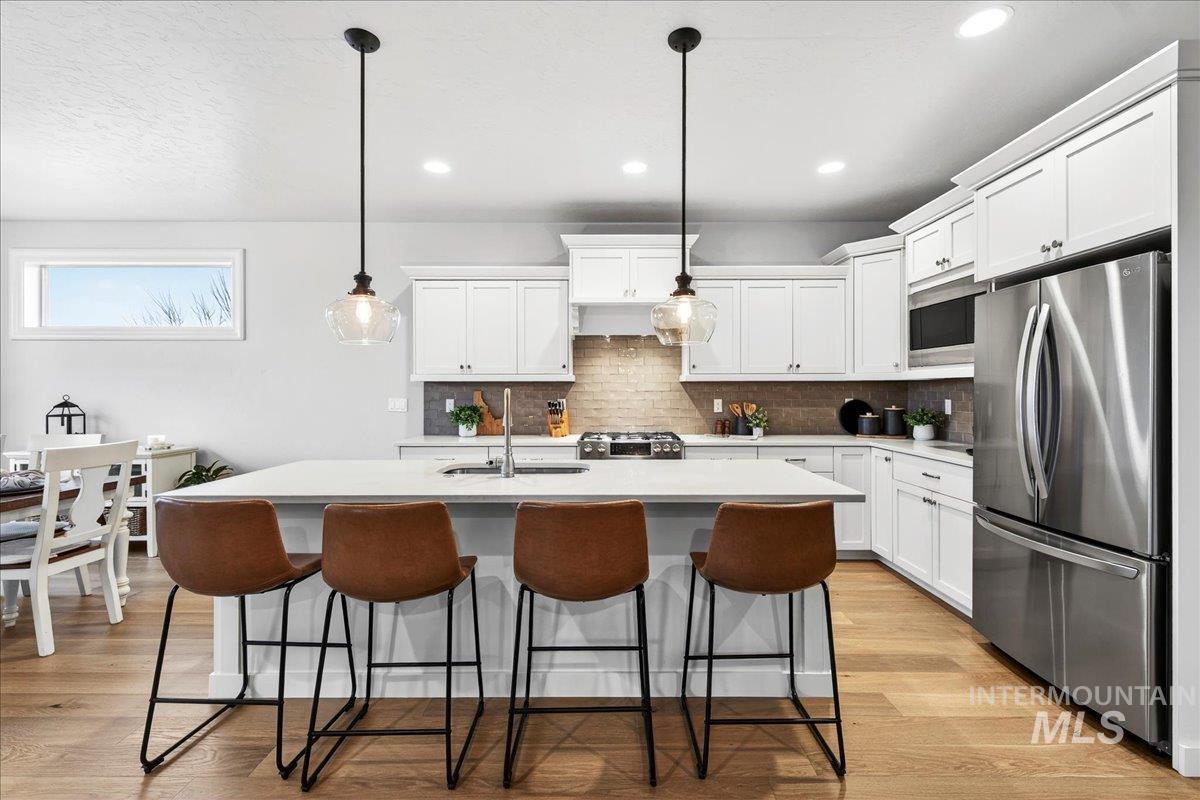 24813 Valley Run Place Star, ID 83669 - Photo 12 of 50 Kitchen with stainless steel appliances, a kitchen island with sink, white cabinetry, pendant lighting, and a breakfast bar