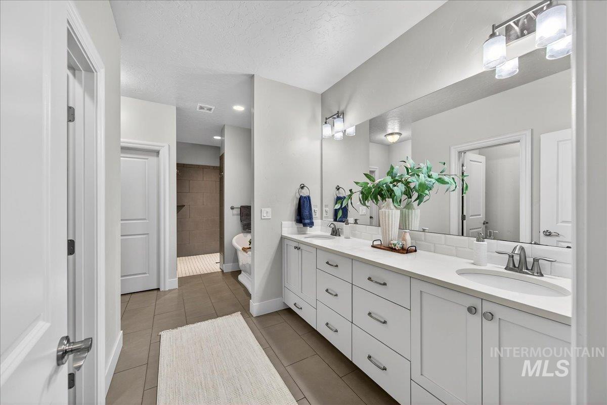 24813 Valley Run Place Star, ID 83669 - Photo 30 of 50 Full bathroom with double vanity, a freestanding bath, a textured ceiling, light tile patterned floors, and walk in shower