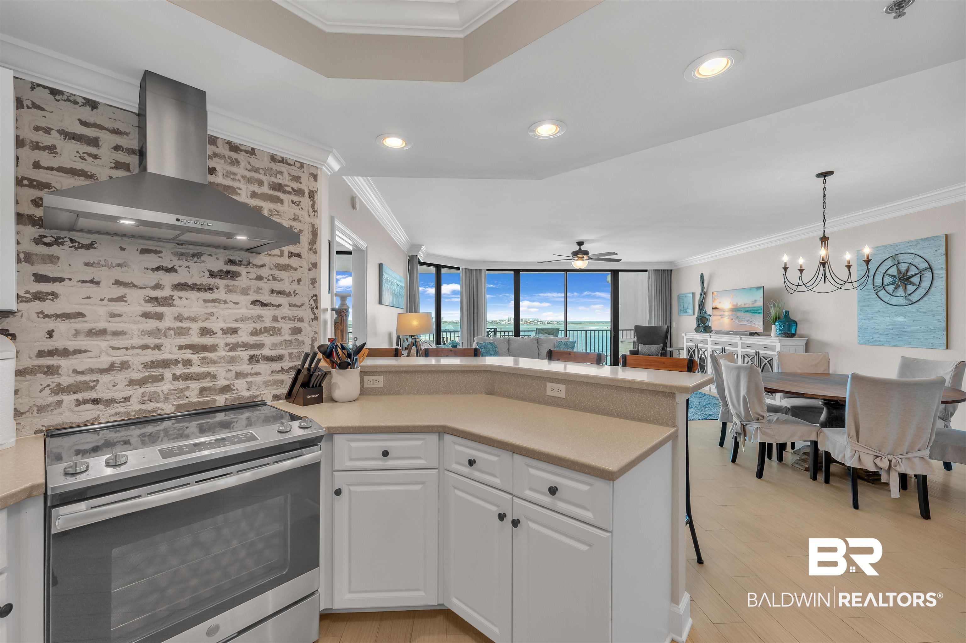 27582 Canal Road, Unit 2605 Orange Beach, AL 36561 - Photo 12 of 41 Kitchen with stainless steel range with electric stovetop, wall chimney exhaust hood, crown molding, a peninsula, and white cabinetry