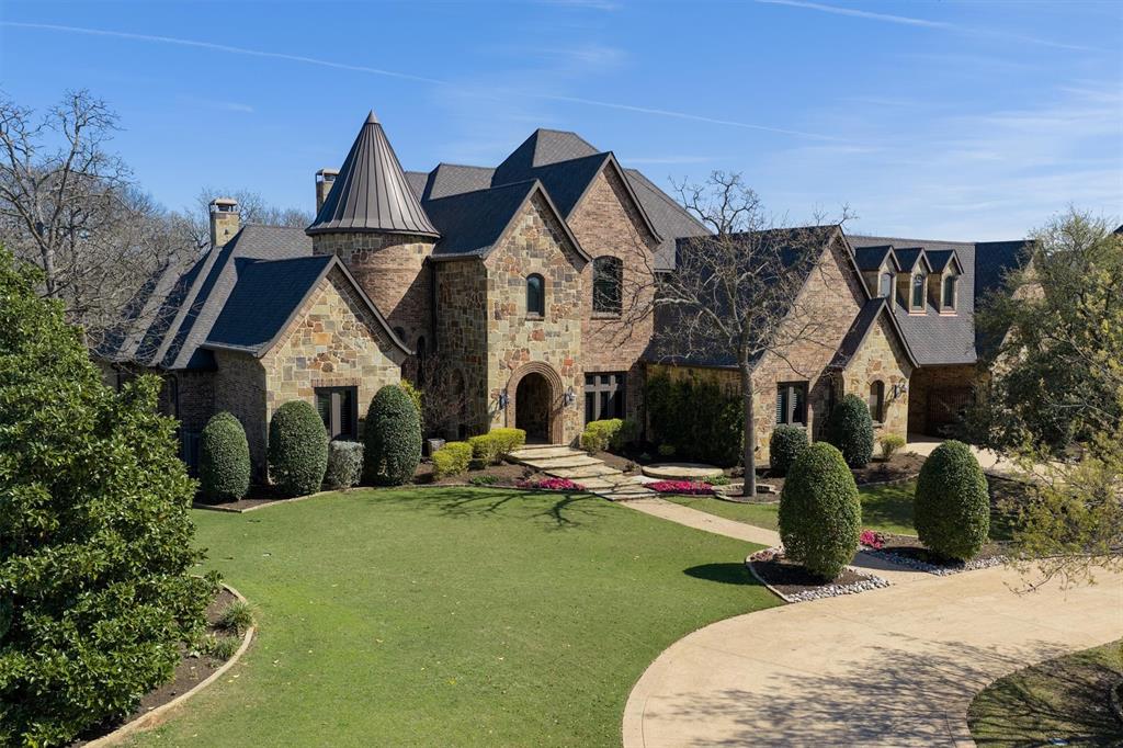 9 Victory Lane Double Oak, TX 75077 - Photo 2 of 40 A closer view of the home showcases its impressive scale, elegant stone and brick exterior, and manicured grounds. Mature trees and lush landscaping enhance the sense of privacy and estate-style living.