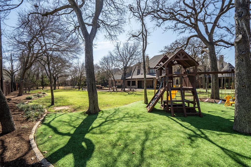 9 Victory Lane Double Oak, TX 75077 - Photo 38 of 40 Children’s play area with swing set and artificial turf offers a dedicated space for outdoor fun. The expansive lawn and mature trees provide plenty of room to relax or play.