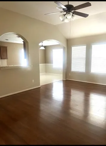 an empty room with wooden floor chandelier fan and windows