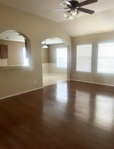 an empty room with wooden floor fan and windows