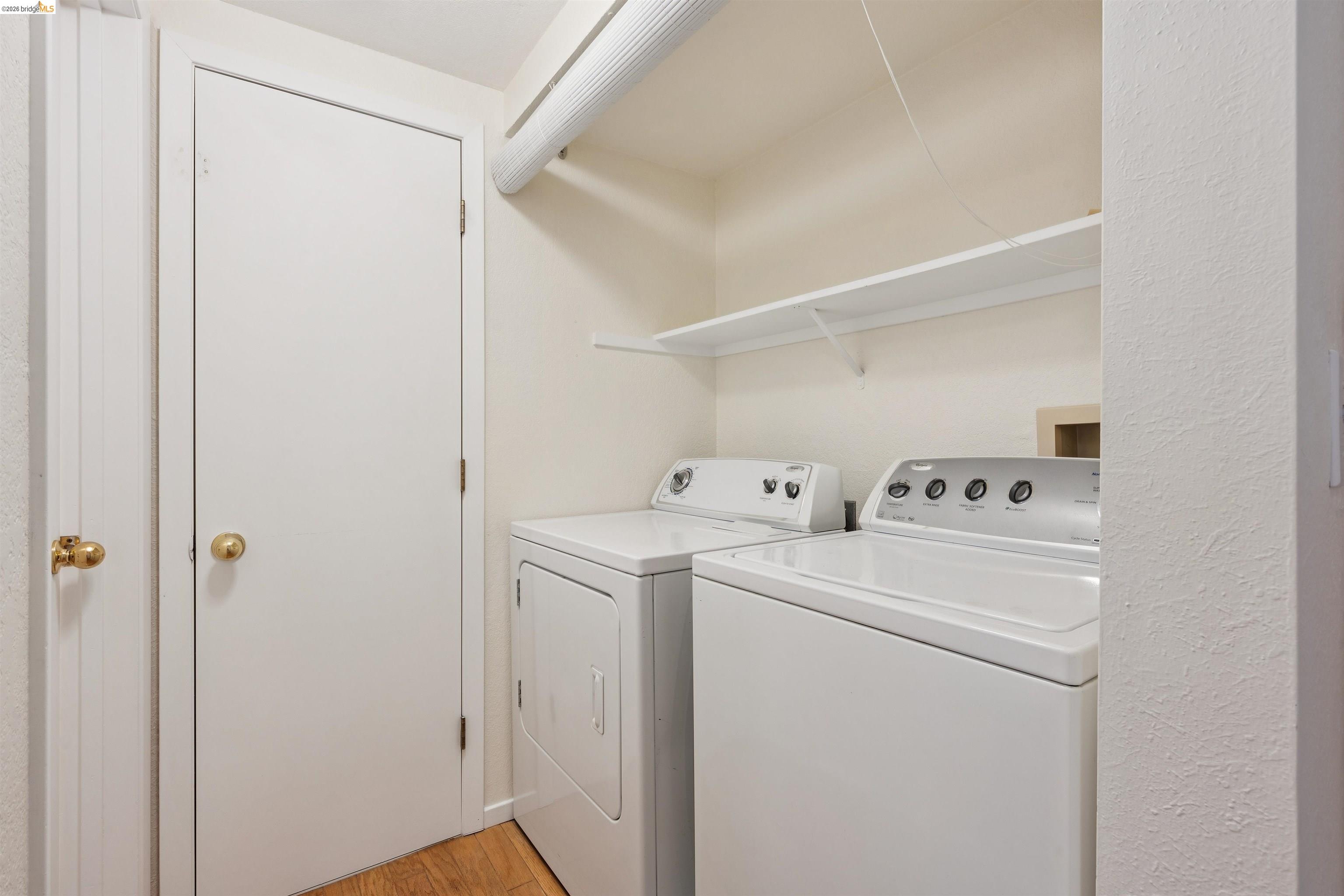 261 Redhawk Road Novato, CA 94949 - Photo 22 of 44 Dedicated laundry space featuring a white washer and dryer, a wall-mounted shelving unit, and wood-finish flooring