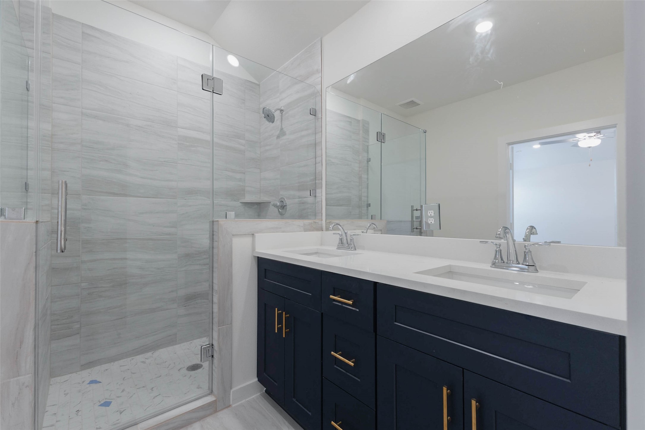 1115 Santee Court Rosharon, TX 77583 - Photo 15 of 23 Here the glass-enclosed shower shows off a pebble-style floor, a corner shelf and a rain-style shower head, designed to feel like a spa at home. The double-sink vanity offers great storage, and the large mirror reflects natural light from the window. Quality finishes and thoughtful details make this a luxurious retreat after a long day at work.