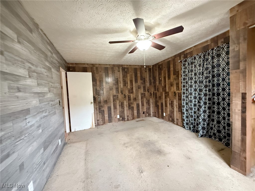 4589 Harmon Creek Road Colliers, WV 26035 - Photo 21 of 26 Spare room featuring wooden walls, a textured ceiling, unfinished concrete flooring, and a ceiling fan