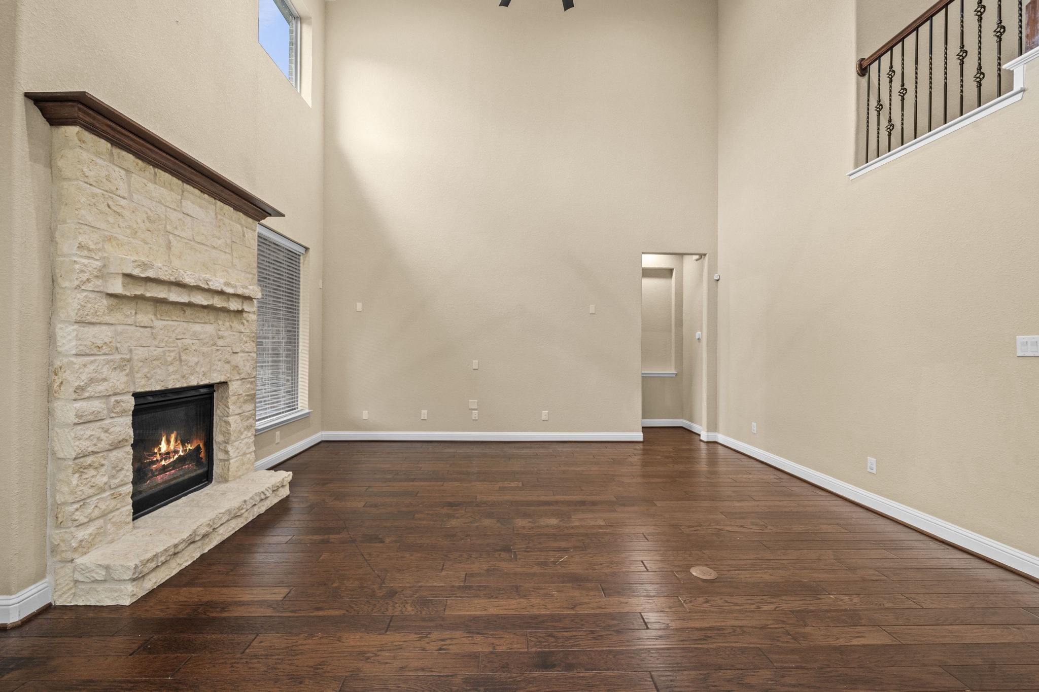 14215 Spindle Arbor Road Cypress, TX 77429 - Photo 12 of 47 Spacious living room with high ceilings, featuring a stone fireplace and rich hardwood floors. Natural light enhances the open feel, with an upper-level railing adding architectural interest. Ideal for cozy gatherings.