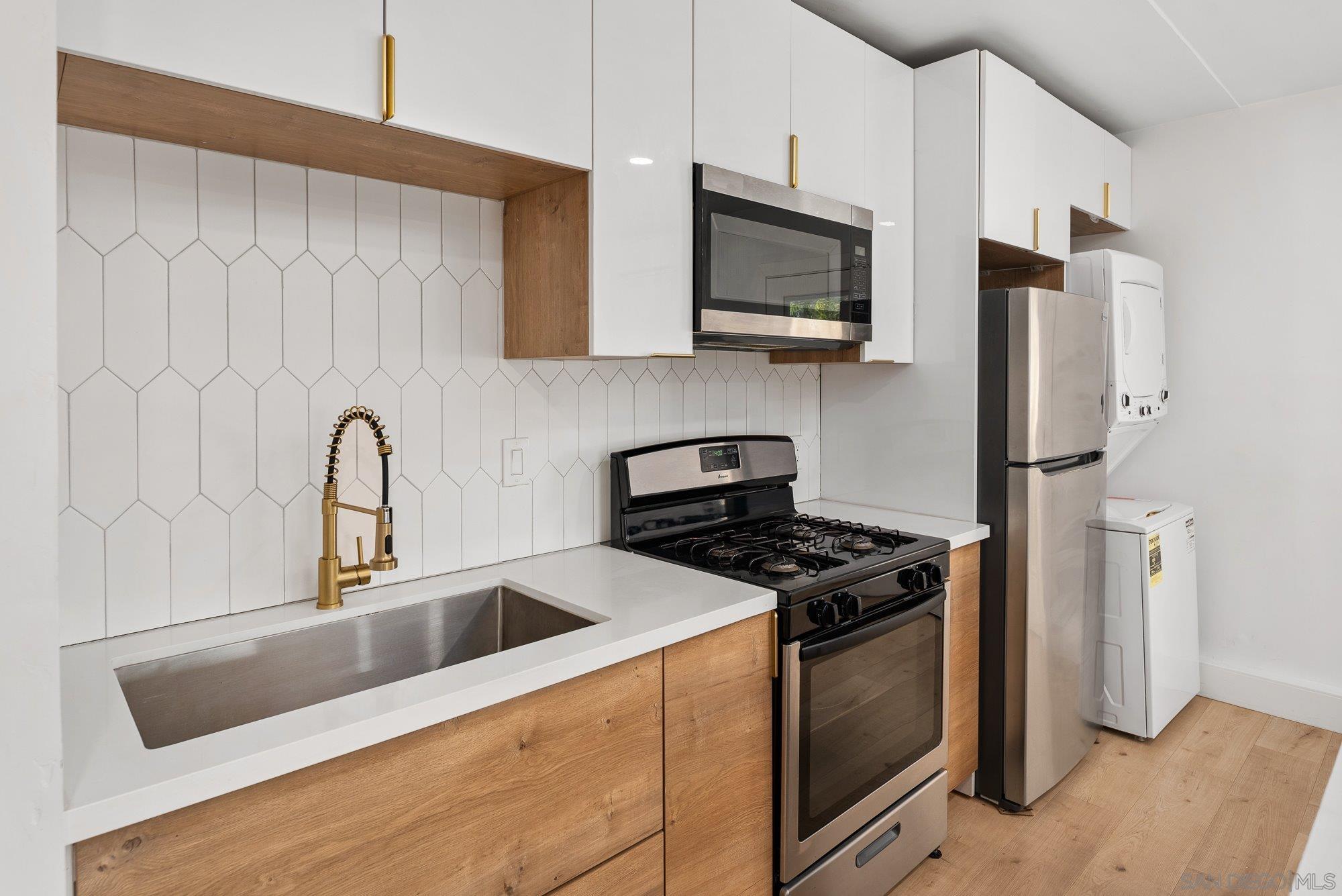 7942 Calico Street San Diego, CA 92126 - Photo 30 of 39 a kitchen with stainless steel appliances granite countertop a sink a stove a refrigerator a microwave oven with white cabinets and a wooden floor