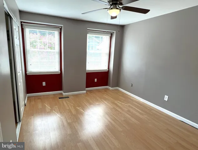 an empty room with wooden floor fan and windows