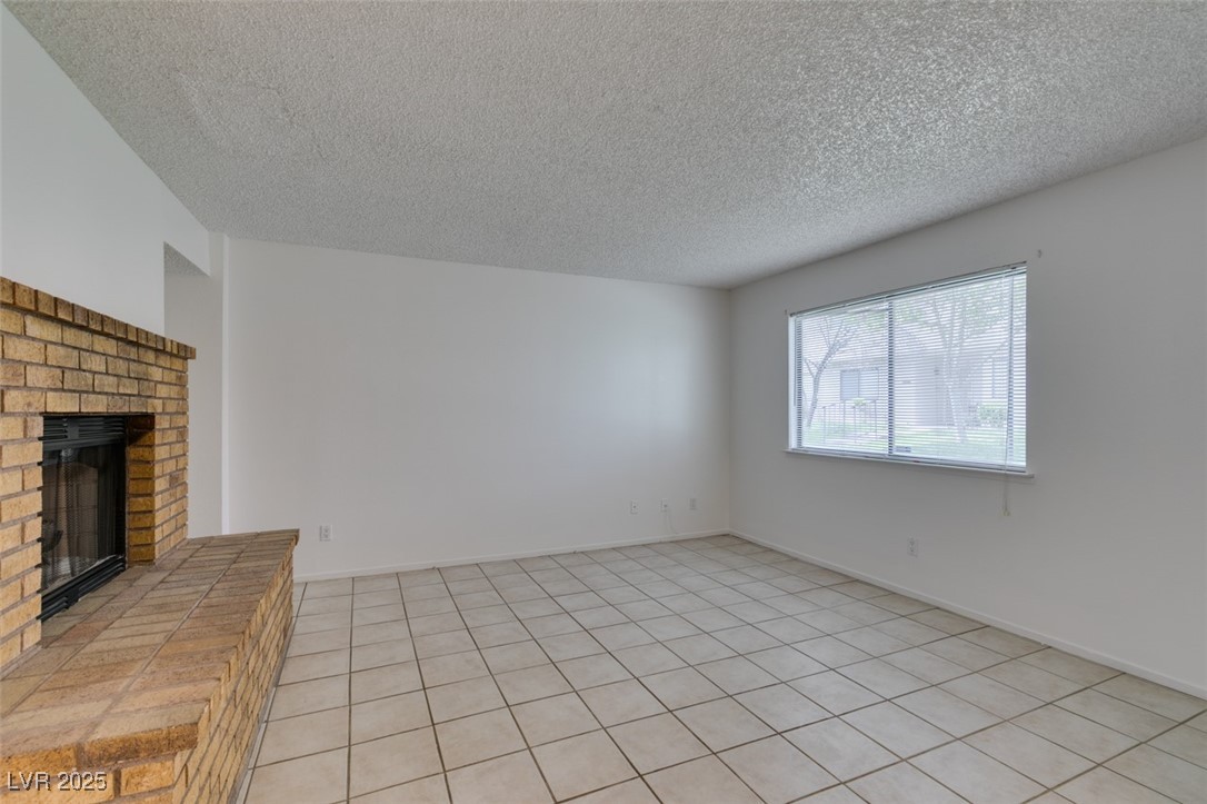 2681 Ruthe Duarte Avenue Las Vegas, NV 89121 - Photo 6 of 43 Unfurnished living room featuring a fireplace, light tile patterned floors, and a textured ceiling