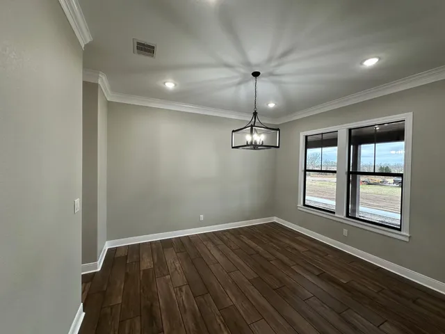an empty room with wooden floor chandelier and windows