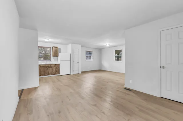 a view of empty room with wooden floor and kitchen