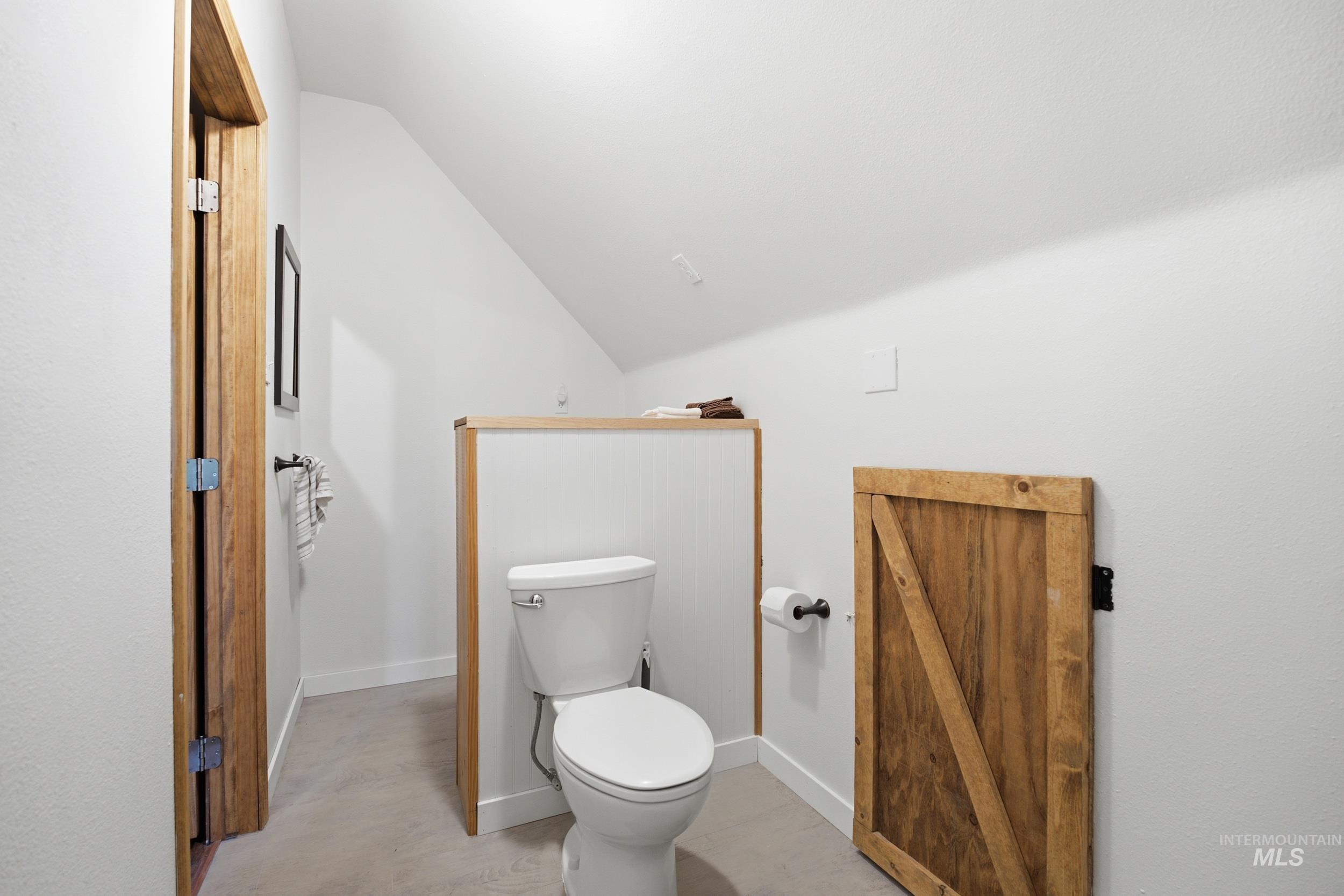 3980 North Pine-Featherville Road Mountain Home, ID 83647 - Photo 29 of 35 Powder room featuring a white two-piece toilet, natural wood-finish trim, and a sloped ceiling