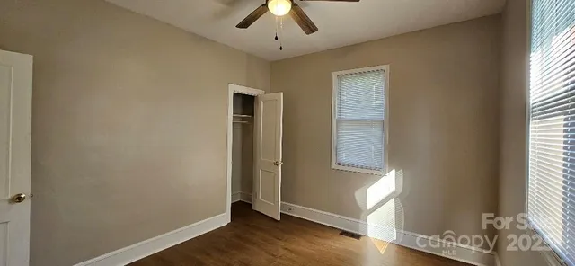 an empty room with wooden floor chandelier fan and windows
