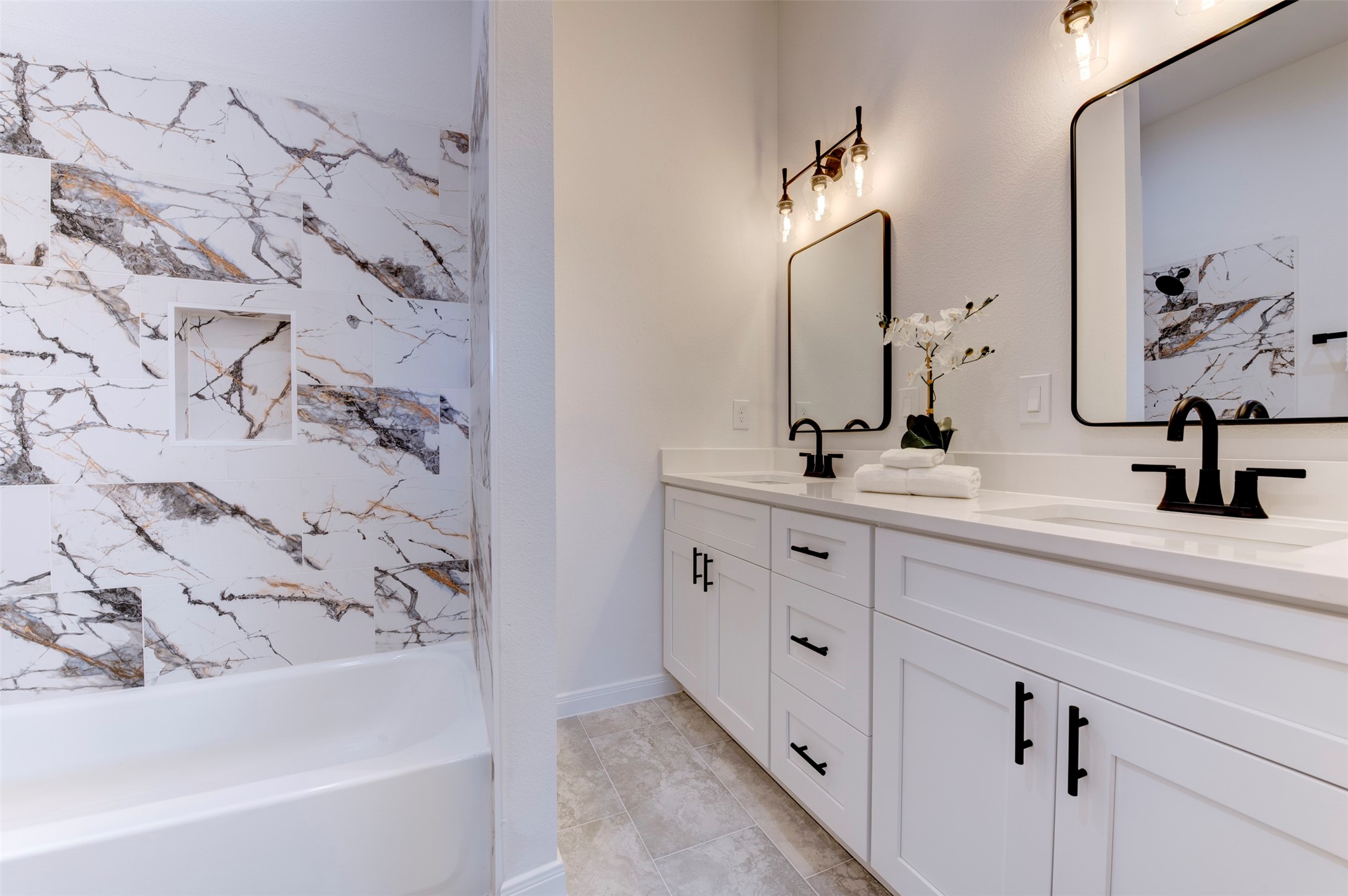 6807 Paris Street Houston, TX 77021 - Photo 37 of 50 Secondary bathroom with double vanity, white shaker cabinets, quartz countertop, matte black fixtures, and floor-to-ceiling marble-look tile surround with built-in niche on tub/shower combo.