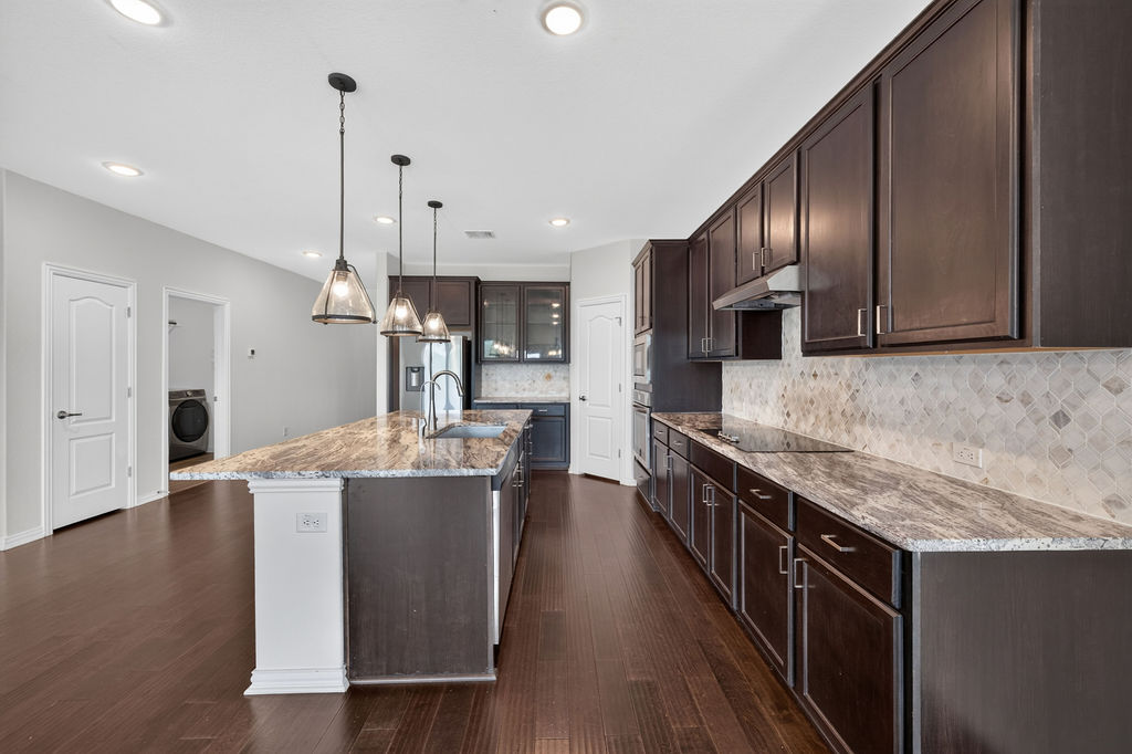 1332 Ridge Runner Drive Georgetown, TX 78628 - Photo 10 of 40 A contemporary kitchen features dark cabinetry, granite countertops, and sleek pendant lighting over a spacious island.