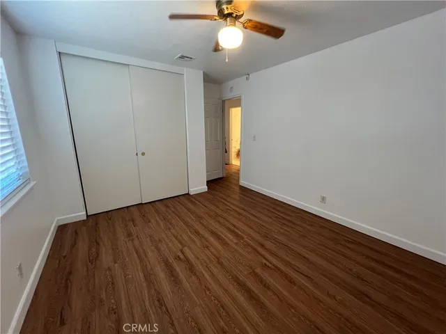 a view of an empty room with wooden floor and a ceiling fan