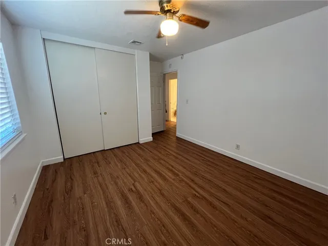 a view of an empty room with wooden floor and a ceiling fan