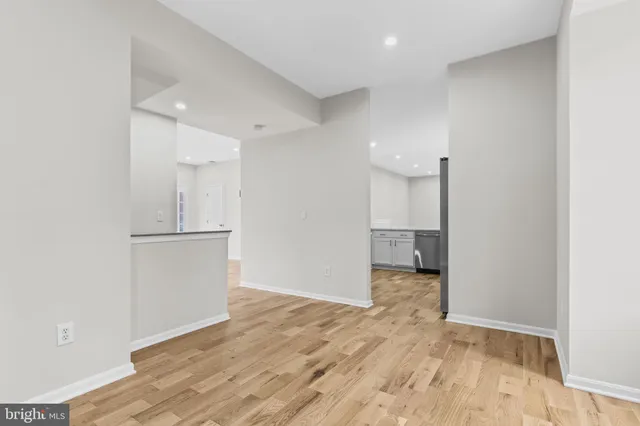 a view of an empty room with wooden floor and kitchen