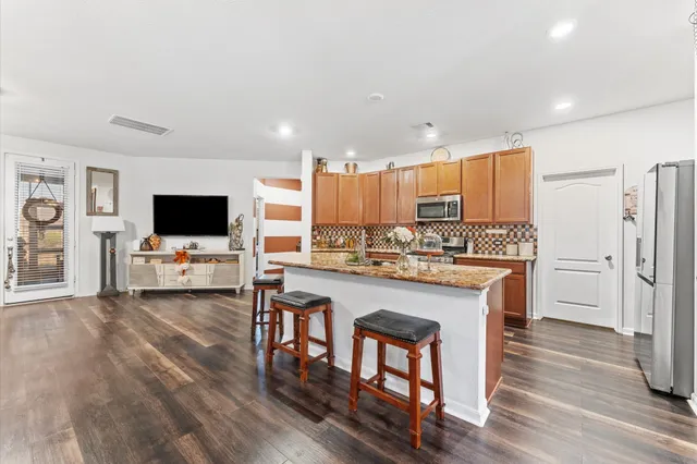 a kitchen with stainless steel appliances a stove top oven a refrigerator a sink and a dining table with wooden floor