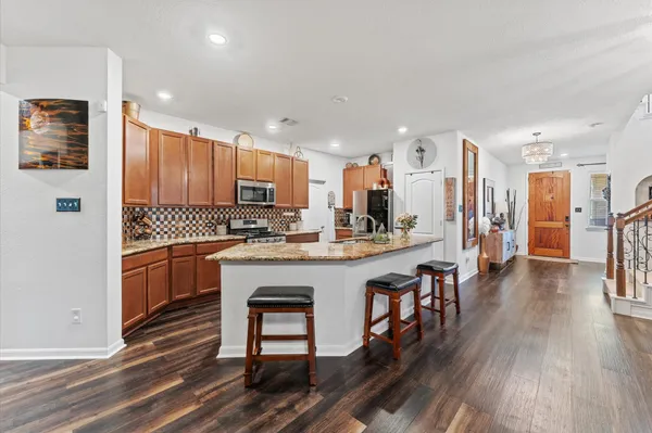 a kitchen with stainless steel appliances granite countertop a refrigerator a stove top oven a sink dishwasher and a dining table with wooden floor