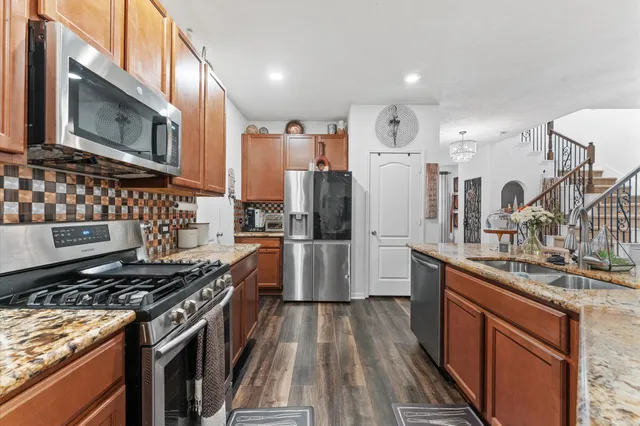 a kitchen with stainless steel appliances granite countertop a stove top oven a sink dishwasher a refrigerator and cabinets with wooden floor