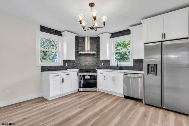 a kitchen with stainless steel appliances granite countertop a refrigerator a sink dishwasher a oven with white cabinets and wooden floor