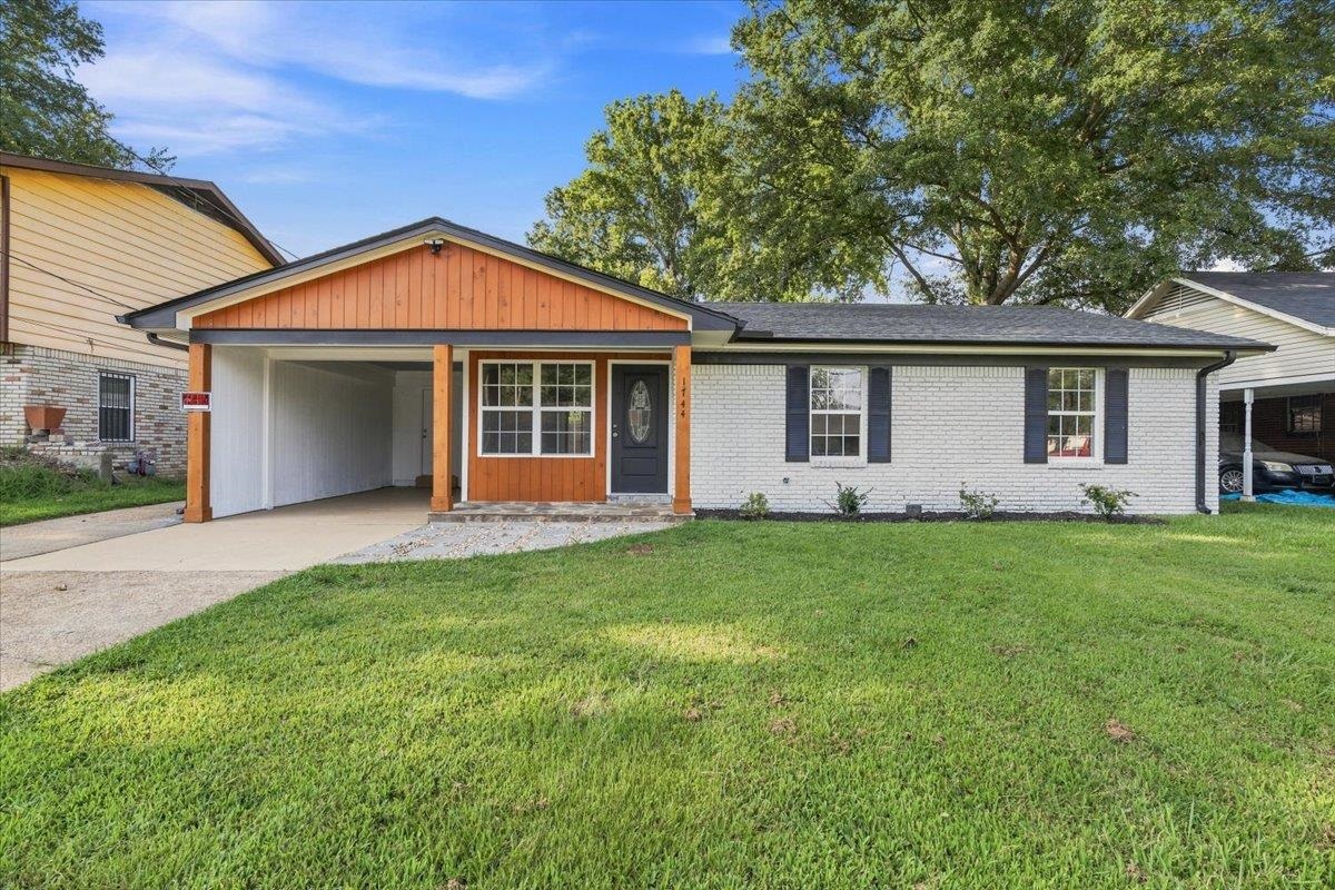 1744 West Holmes Road Memphis, TN 38109 - Photo 1 of 24 White brick exterior, wood siding accents, dark gray entry door, covered carport, and a manicured lawn