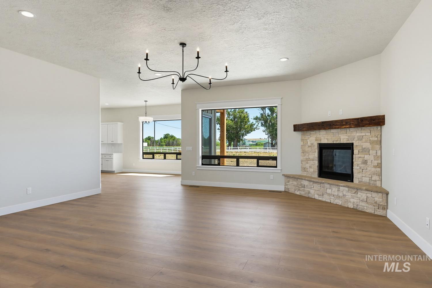5054 Heritage Drive Marsing, ID 83639 - Photo 16 of 38 Spacious living area featuring wood-finish flooring, a corner stone fireplace with a rustic wood mantel, and expansive windows